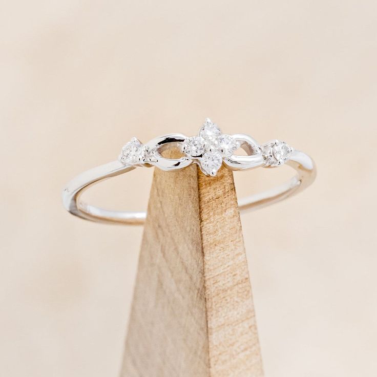 a three stone diamond ring sitting on top of a wooden stand