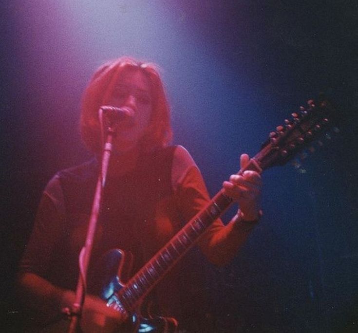 a woman holding a guitar while standing in front of a microphone