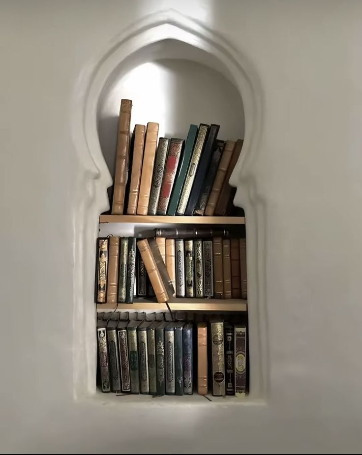 a book shelf filled with lots of books on top of a white wall next to a window