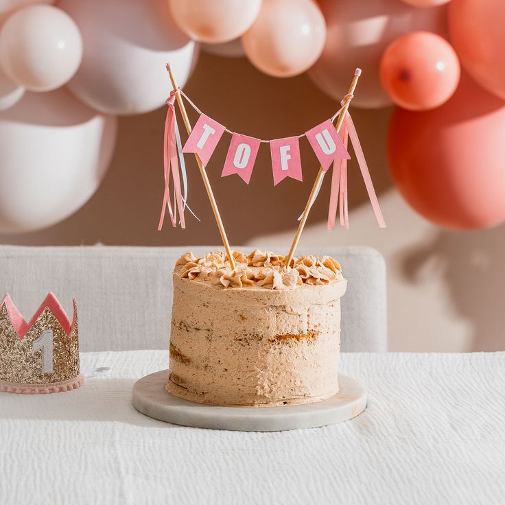 a cake on a table with pink and white balloons in the background that say mom