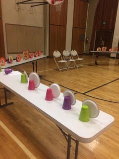 a long table with colorful cups on it in an empty gym area at the end of a basketball court