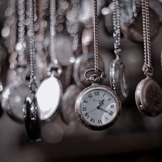 an antique pocket watch hanging from chains in front of many other watches and necklaces