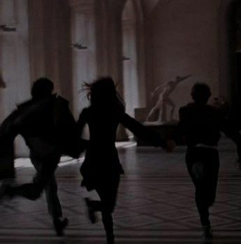 three people are running in the middle of a room with large columns and stone pillars