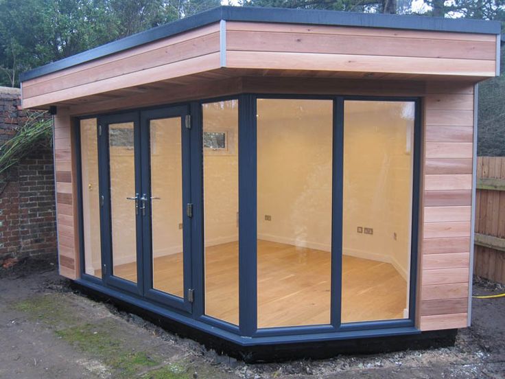 a small wooden building with sliding glass doors on the inside and outside side, in a garden area