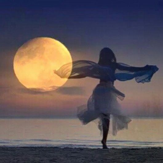 a woman standing on top of a beach under a full moon