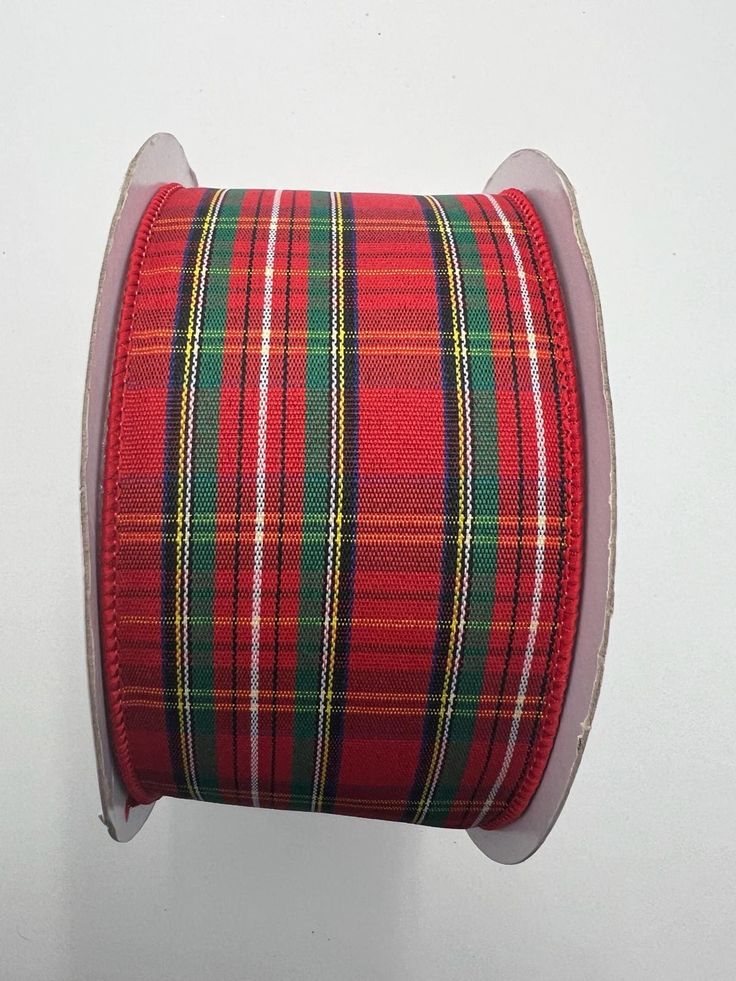 a spool of red and green plaid ribbon on a white background with a pink edge