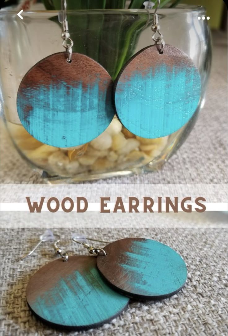 two wooden earrings with blue and brown paint on them sitting in front of a vase filled with flowers