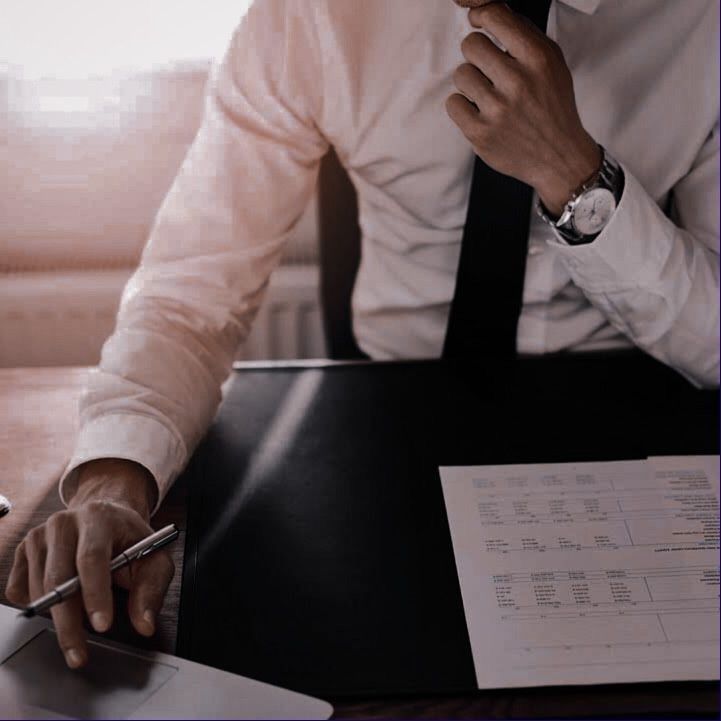 a man sitting at a desk with a pen and paper in his hand while using a laptop computer