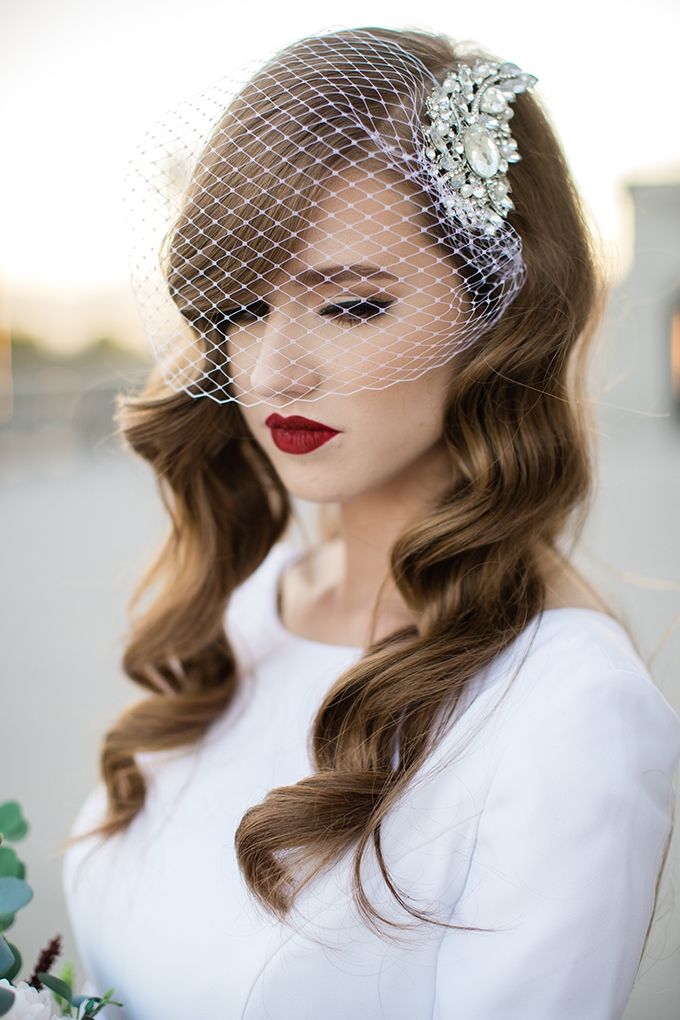 a woman with long hair wearing a veil and holding a flower in her hand while looking at the camera