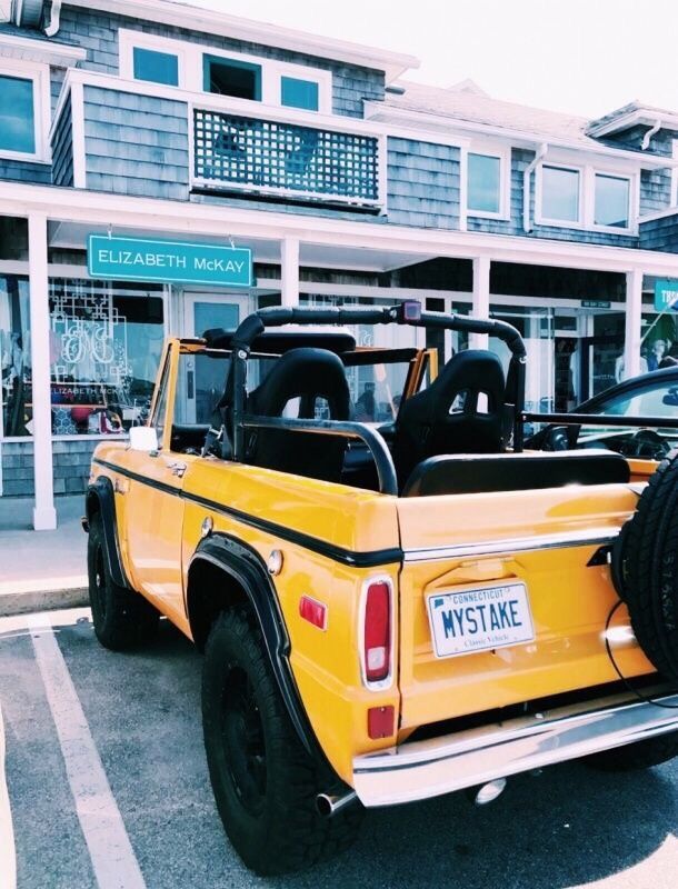 a yellow pick up truck parked in front of a building with two large tires on it's flatbed