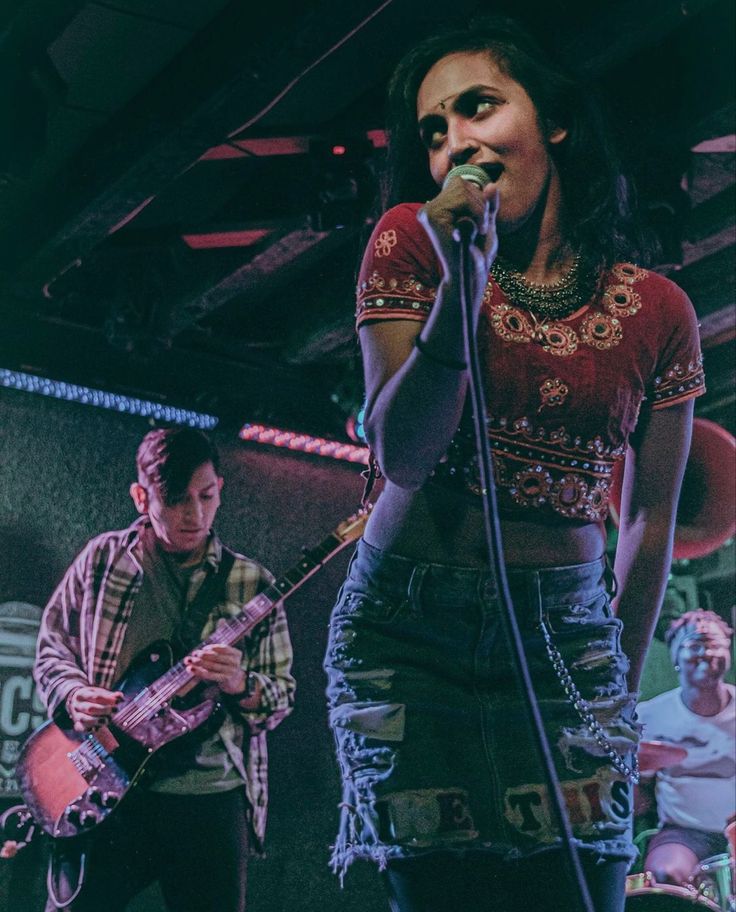 a woman singing into a microphone while standing next to a man with a guitar on stage