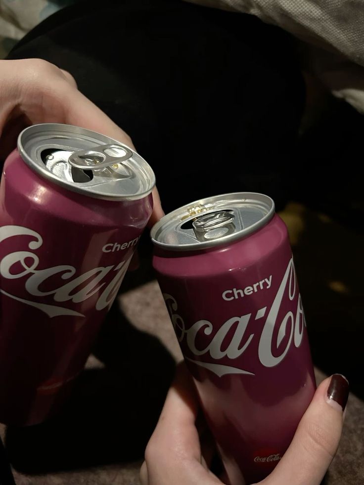 two cans of coca - cola are being held by someone