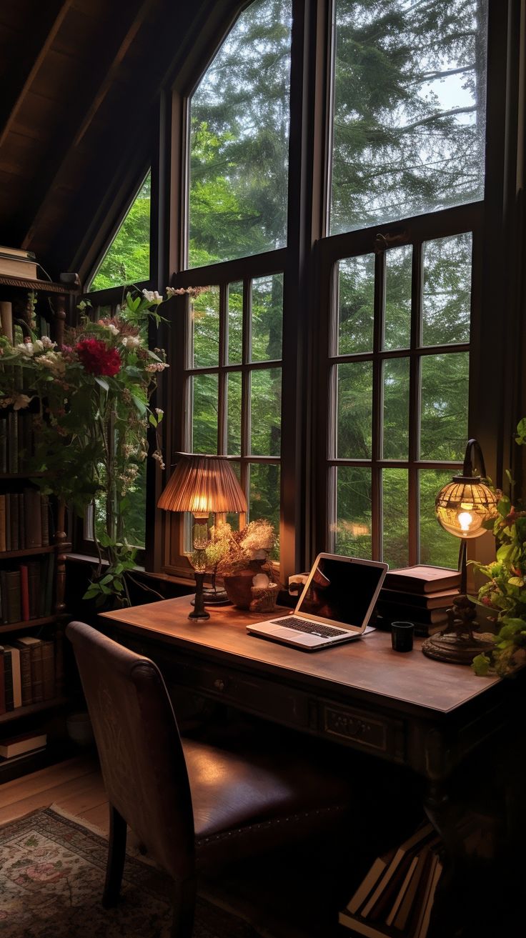 a desk with a lamp on it in front of two large windows that look out onto the woods