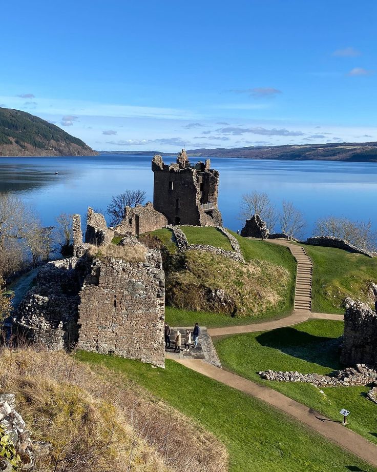 an old castle sitting on top of a lush green hillside next to a body of water