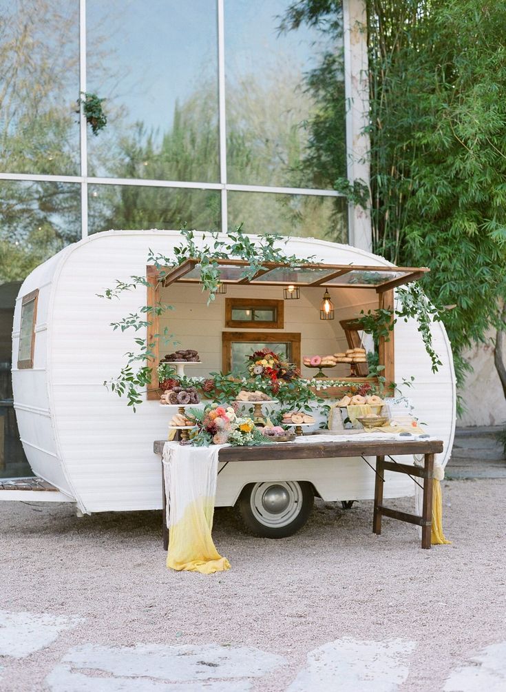 an old camper converted into a food truck with flowers and greenery on the back