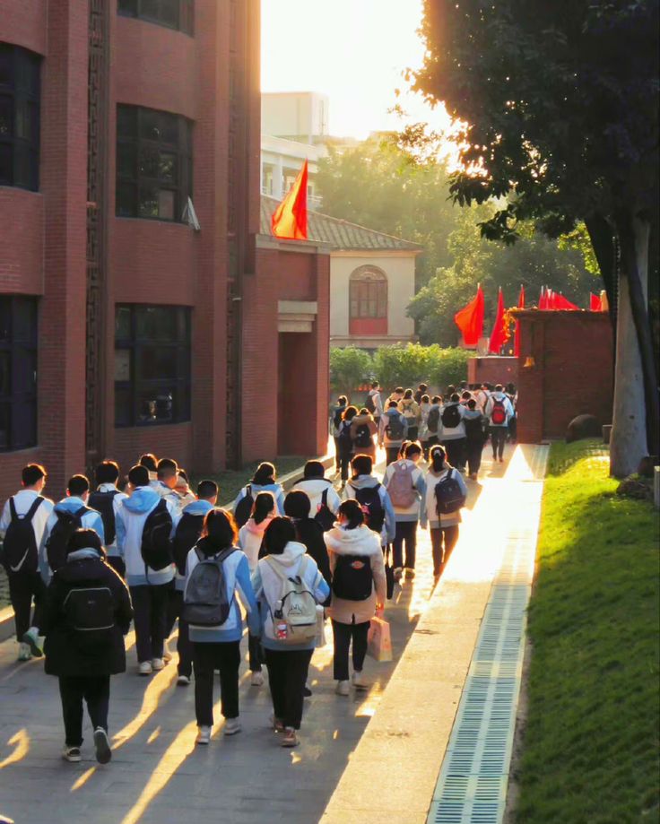 a group of people walking down a sidewalk in front of a tall building with red flags on it