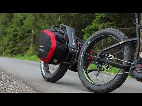 a person riding a bike down a road with a bag attached to the front wheel