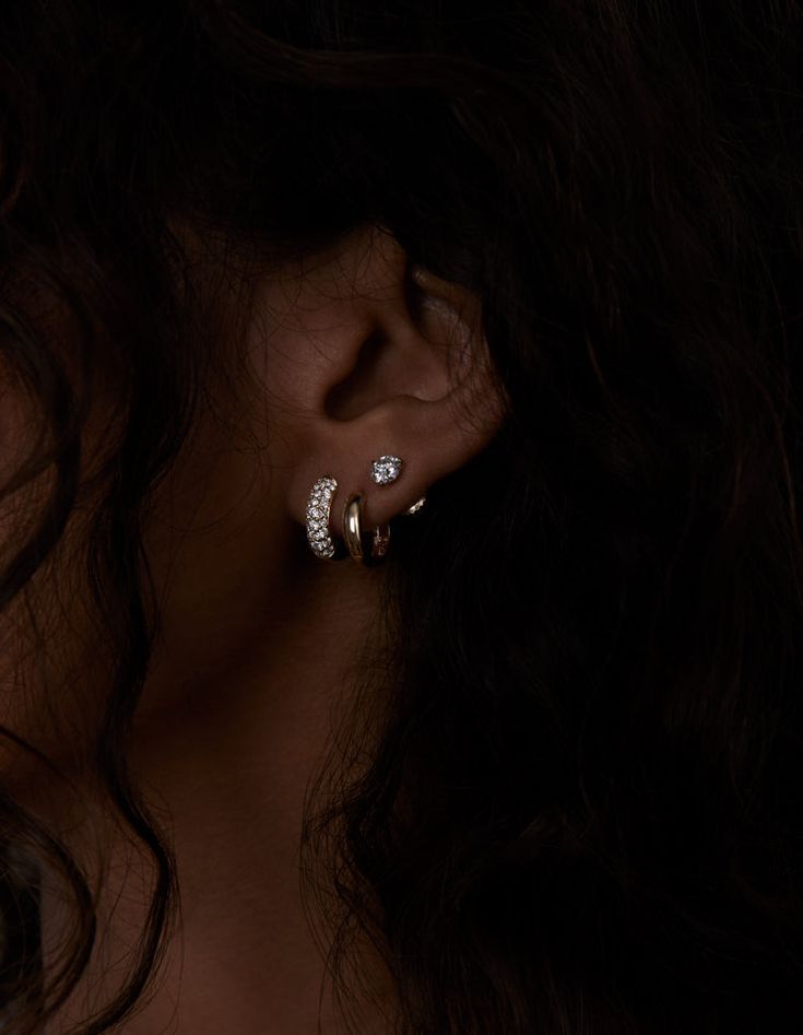 a close up of a woman's ear wearing gold and diamond hoop earrings, with dark background