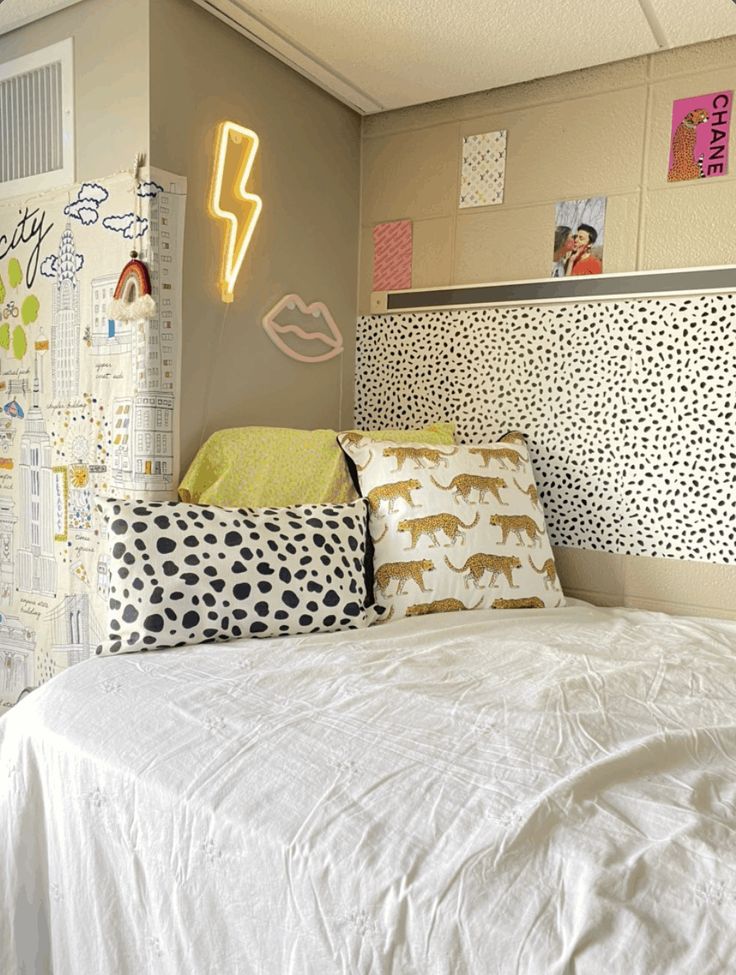 a white bed topped with lots of pillows next to a wall mounted neon light sign