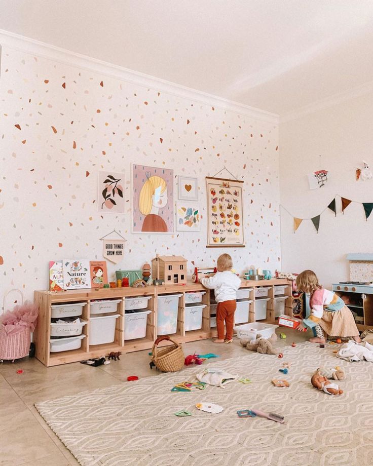 two young children playing in a playroom with toys on the floor and wallpaper