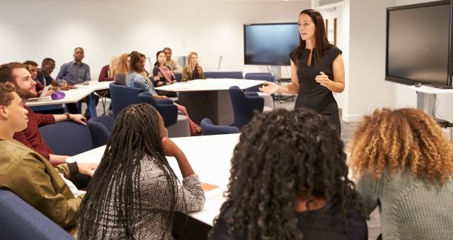 a woman standing in front of a class room full of women sitting at desks