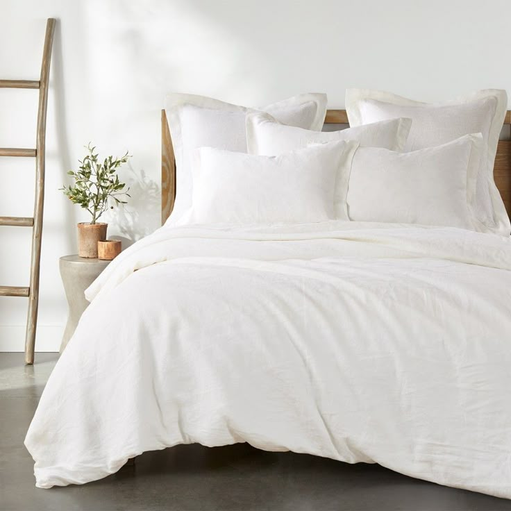 a bed with white linens and pillows in a room next to a wooden ladder