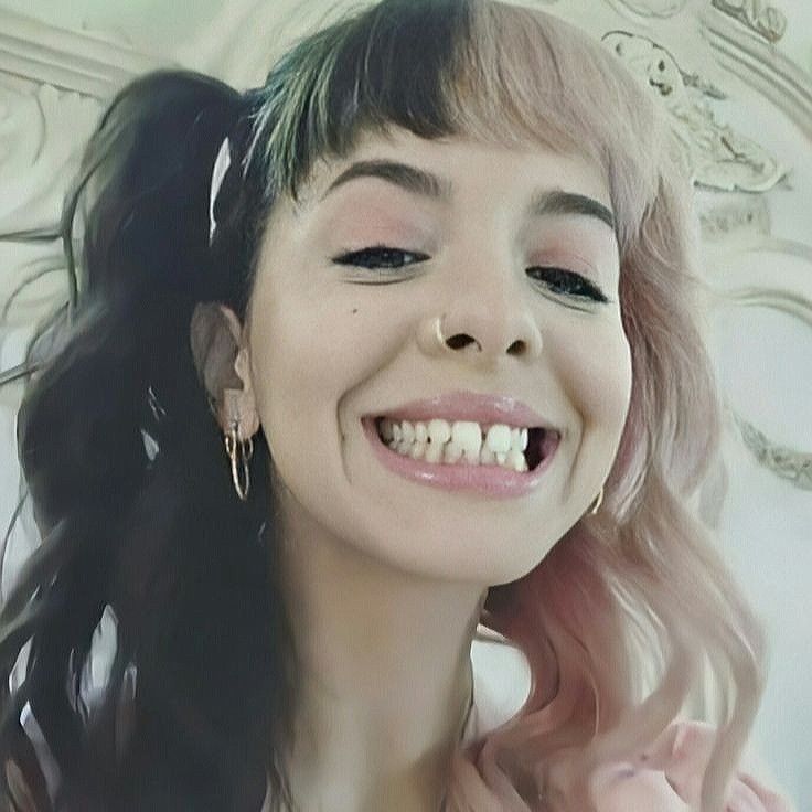 a smiling woman with long hair and piercings on her ears, wearing gold hoop earrings