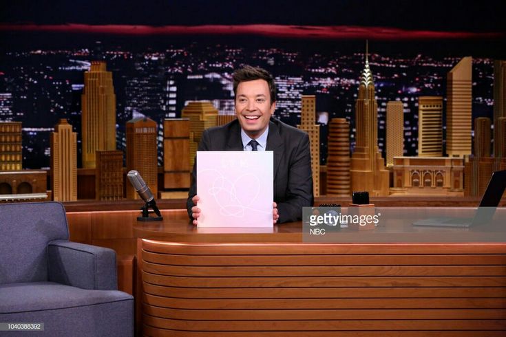 the tonight show host holding up a piece of paper while sitting in front of his desk