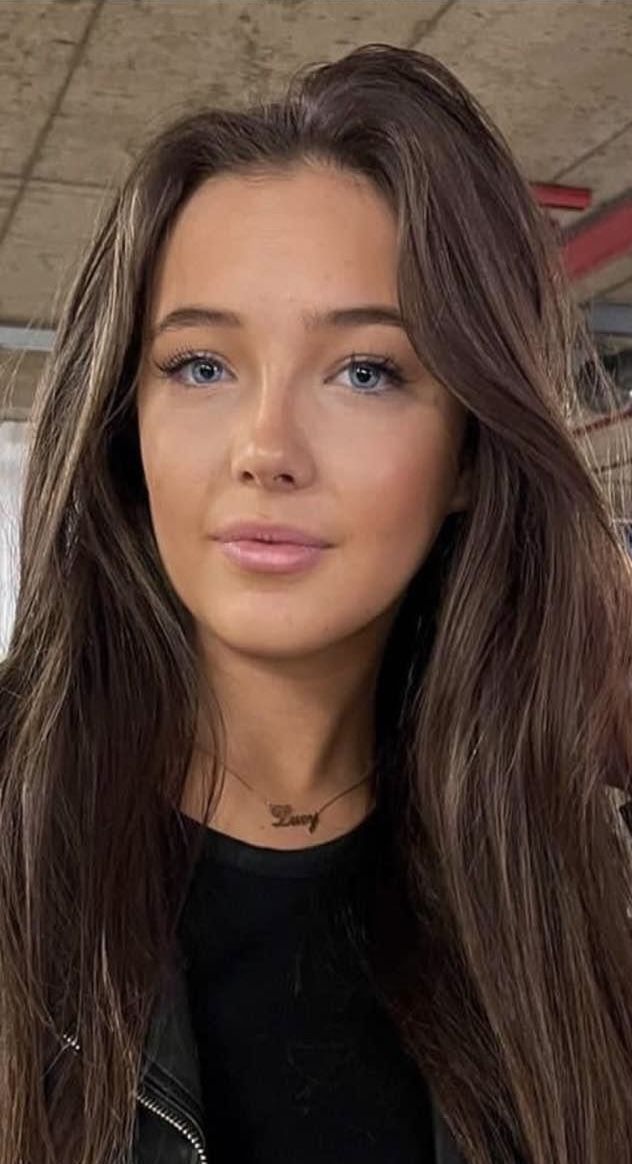 a woman with long brown hair wearing a black shirt and leather jacket is looking at the camera