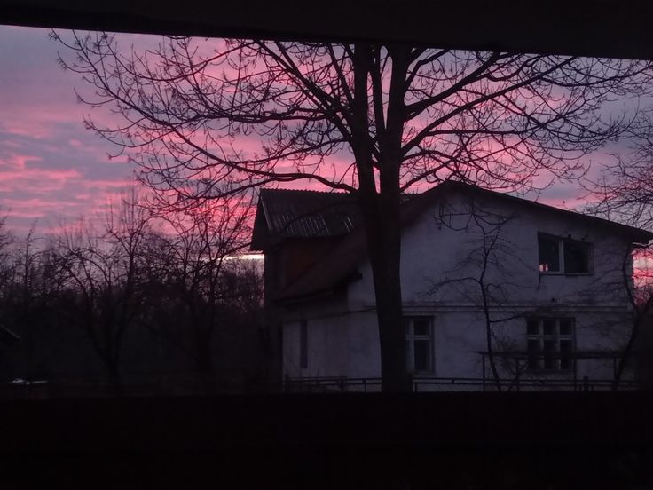 the sky is pink and purple as the sun sets in the distance behind a house