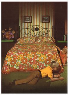 two people laying on the ground in front of a bed with an orange and yellow bedspread