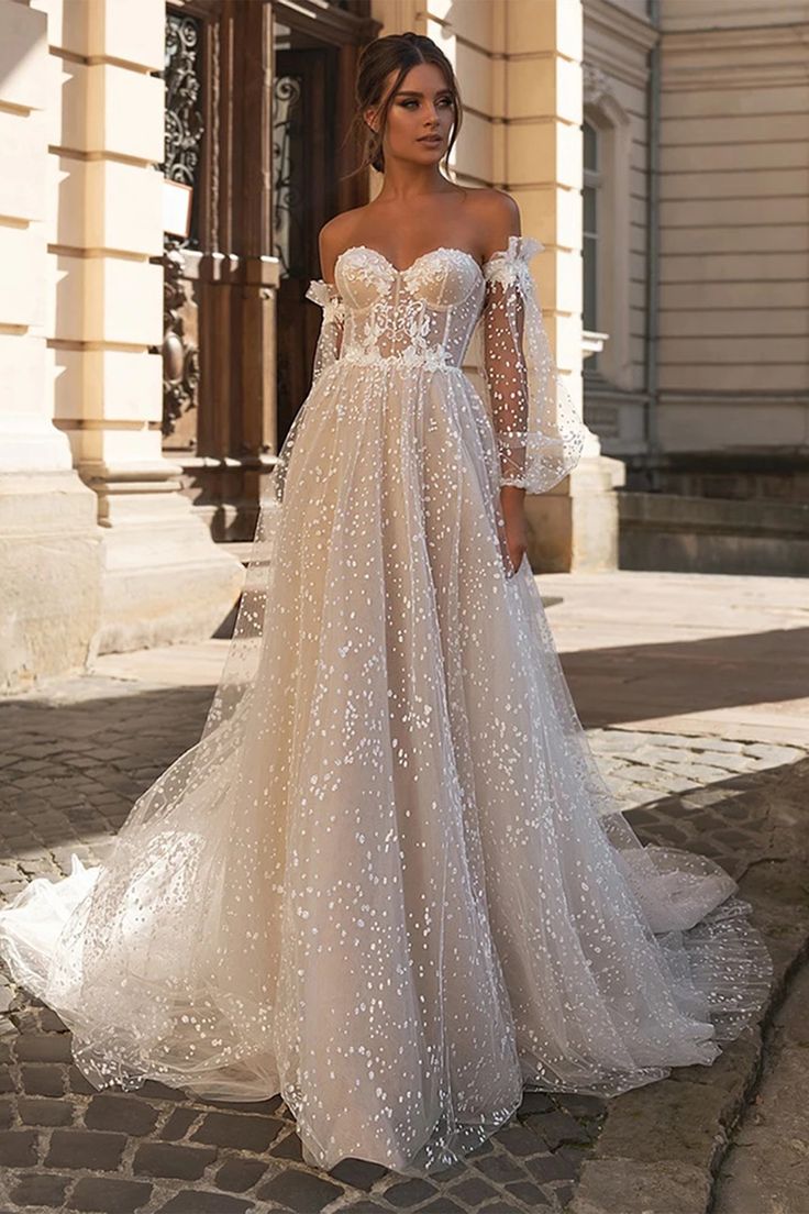 a woman in a wedding dress standing on a cobblestone street wearing an off the shoulder gown