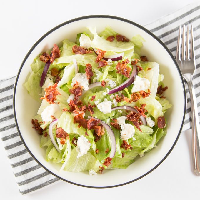 a white bowl filled with lettuce and bacon on top of a striped napkin