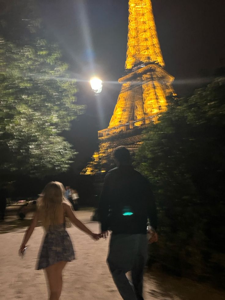 a man and woman holding hands in front of the eiffel tower at night