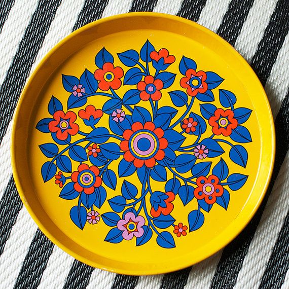 a yellow plate with blue, red and orange flowers on it sitting on a black and white striped tablecloth