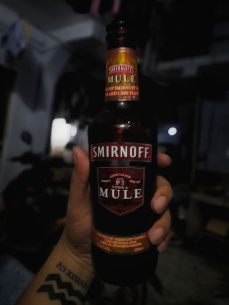 a person holding up a bottle of beer in their left hand, with the word smirnoff on it