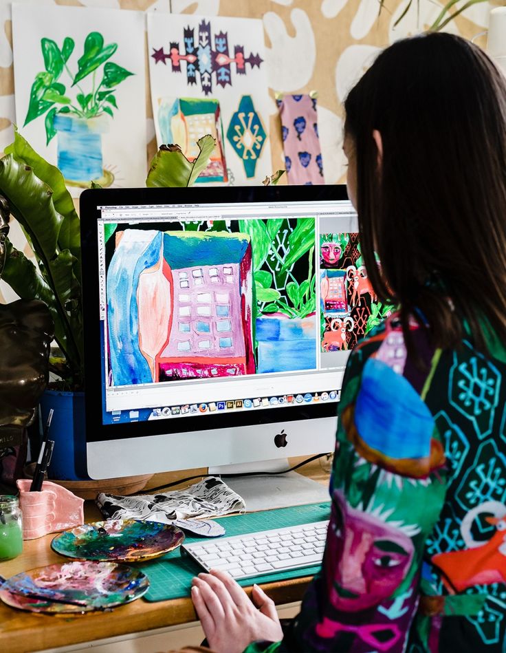 a woman sitting at a desk in front of a computer monitor with an art work on it