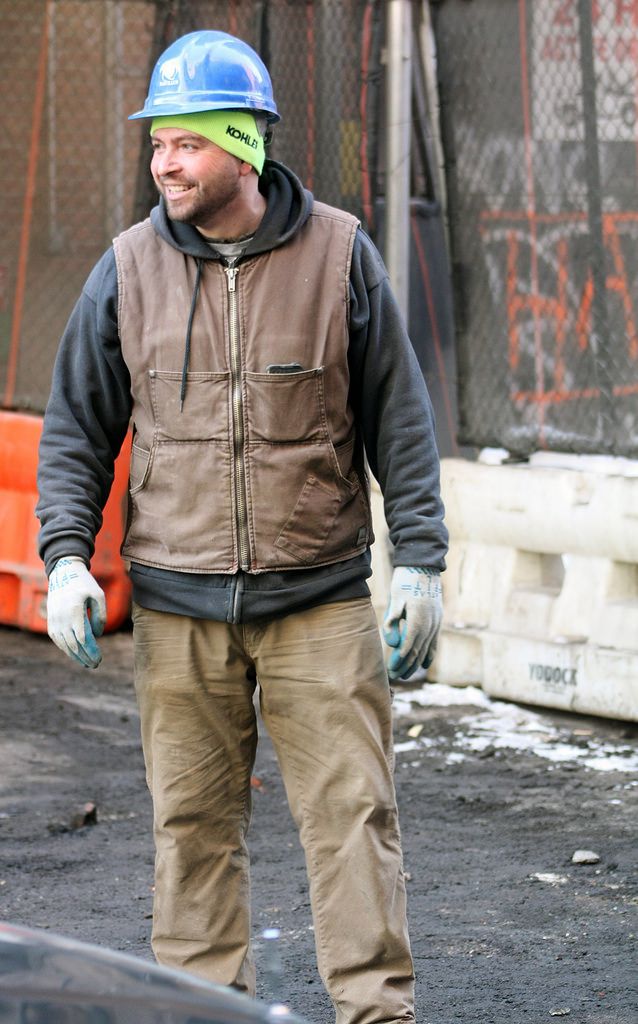 a man wearing a helmet and gloves standing in front of a building with a skateboard