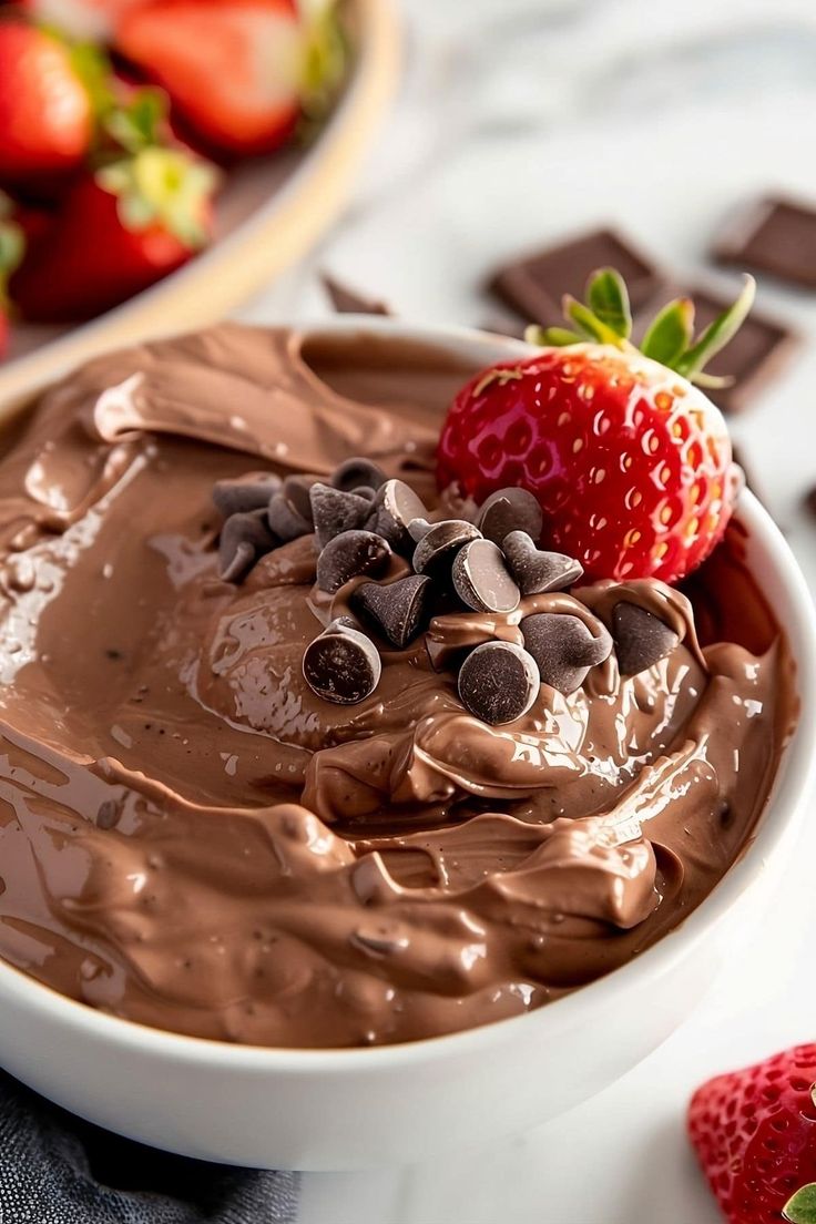 a bowl filled with chocolate and strawberries on top of a white table next to another bowl