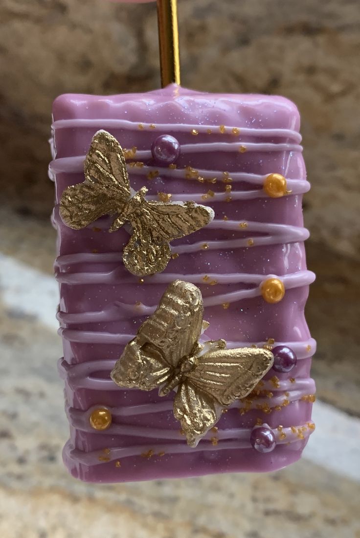 a purple candle with gold butterflies hanging from it's side on a stick in front of a stone wall