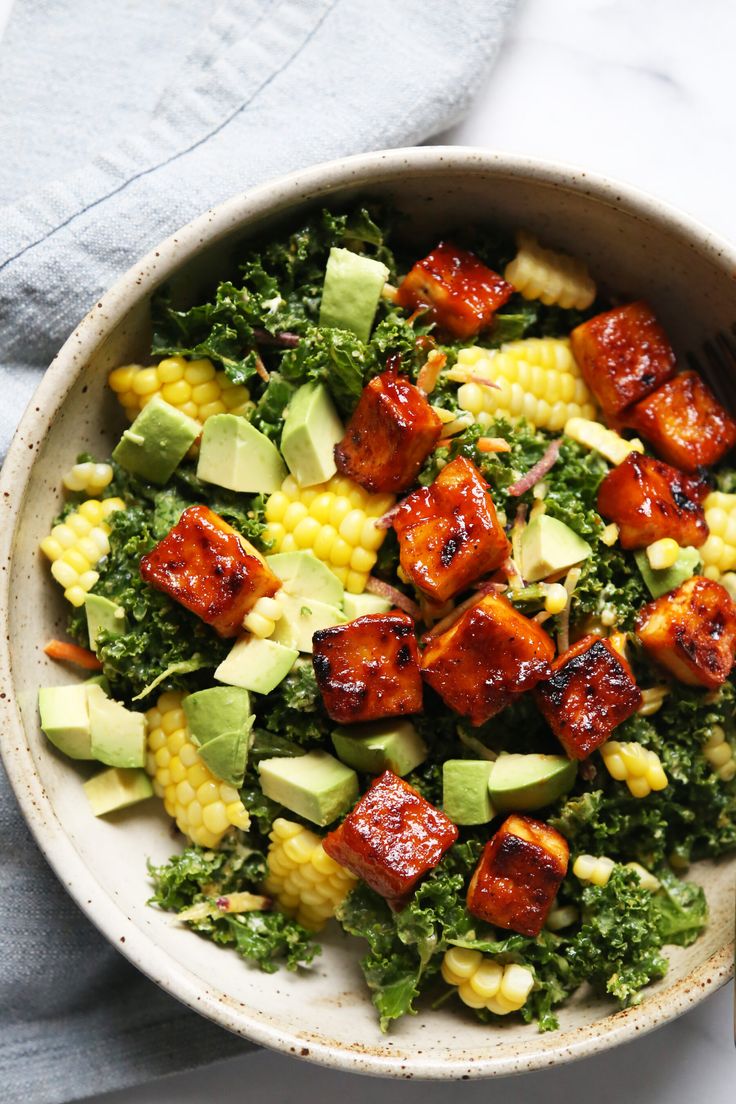 a bowl filled with vegetables and tofu on top of a blue towel next to a fork