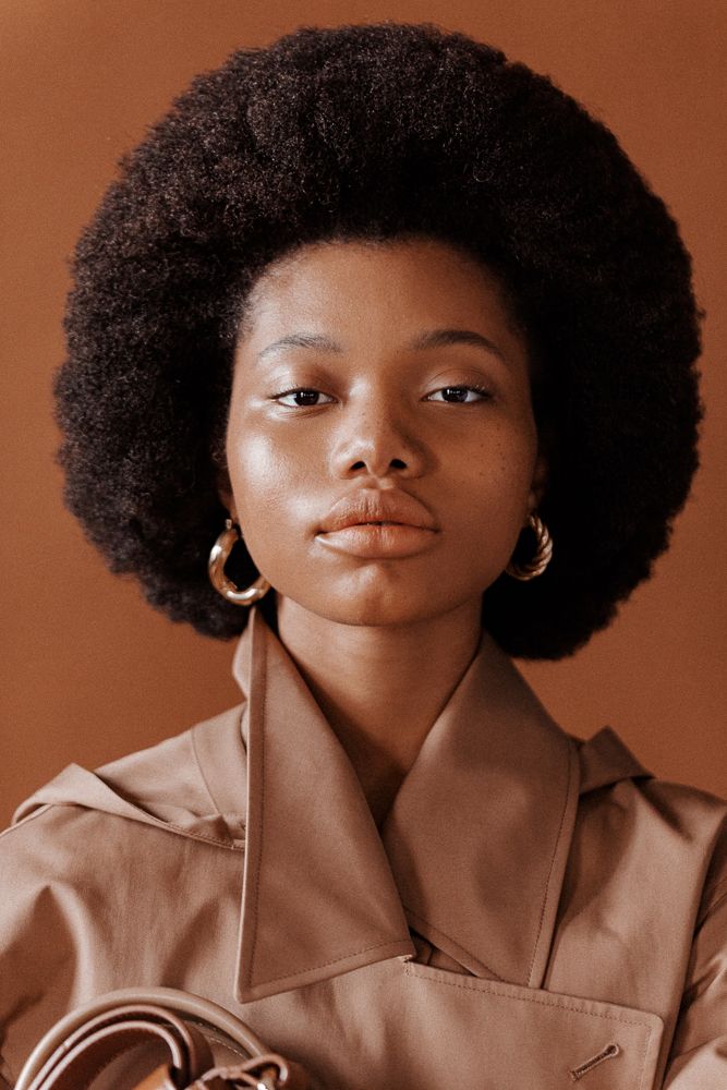 a woman with an afro holding a handbag in her right hand and looking at the camera