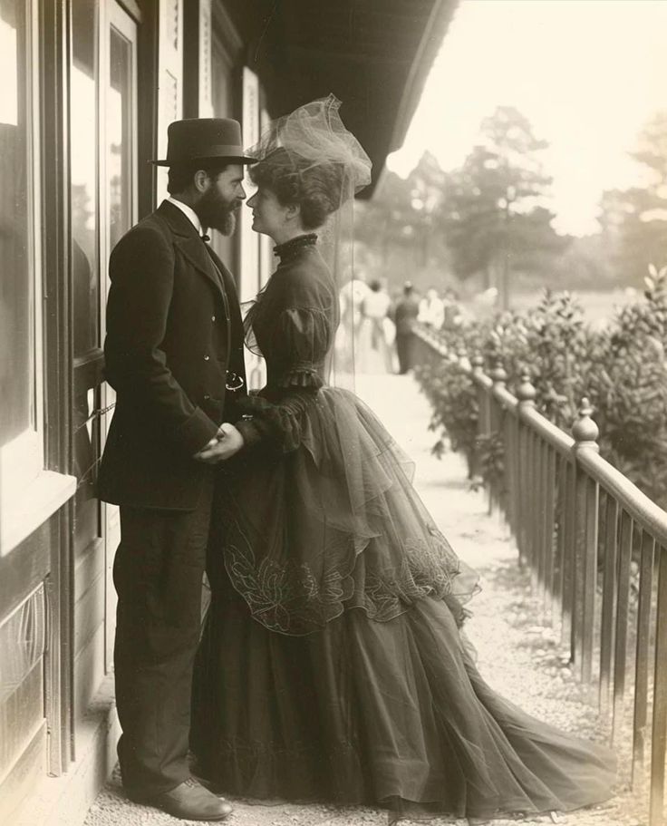 an old black and white photo of a man and woman in formal wear standing on a porch