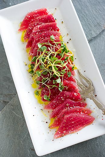 a white plate topped with slices of fish covered in sauce and garnished with sprouts