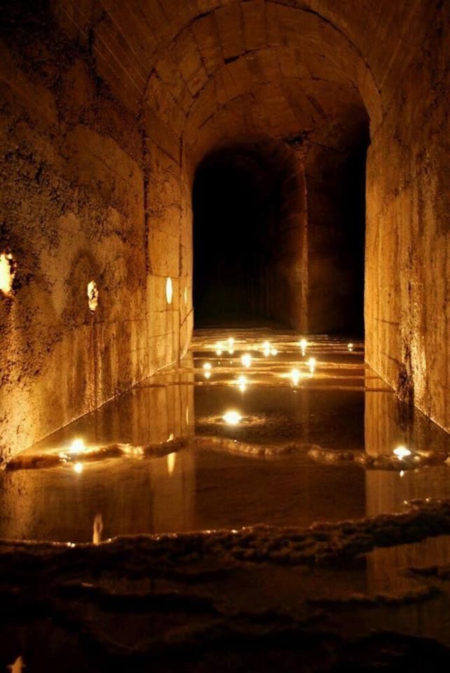 candles are lit in an old tunnel with water running down the side and on the floor