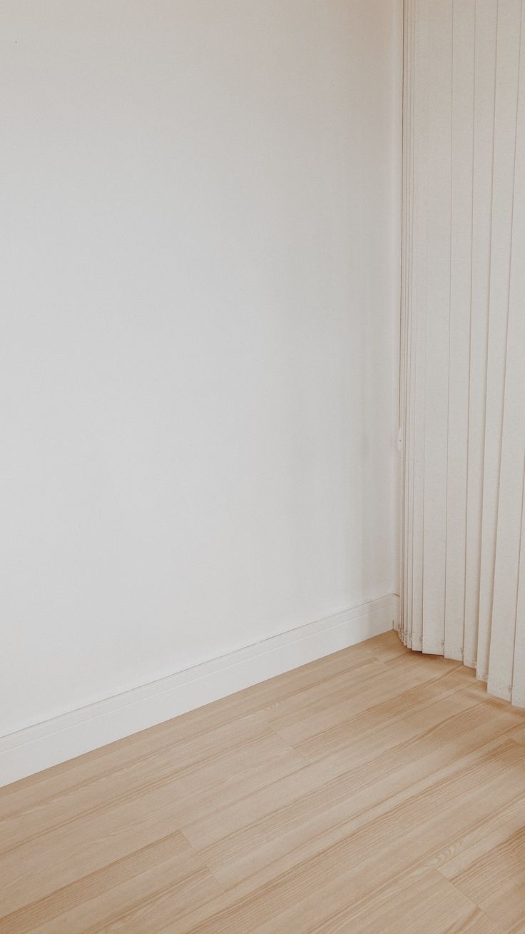 an empty room with white walls and wood flooring is pictured in this image from the corner