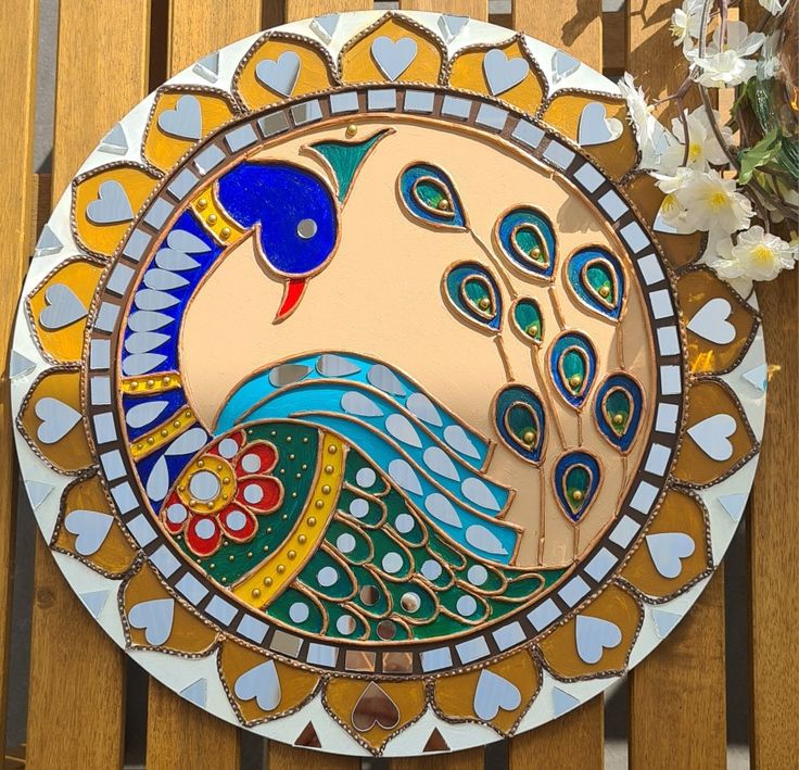 a decorative plate with a peacock on it sitting on a wooden table next to flowers