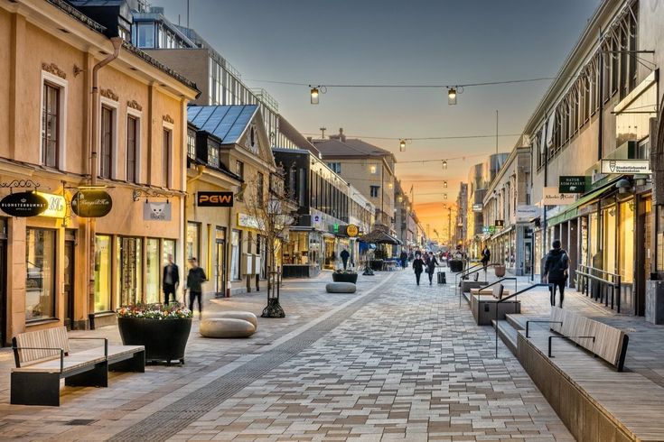 people are walking down the street in an old town at sunset or dawn, with shops and stores on either side