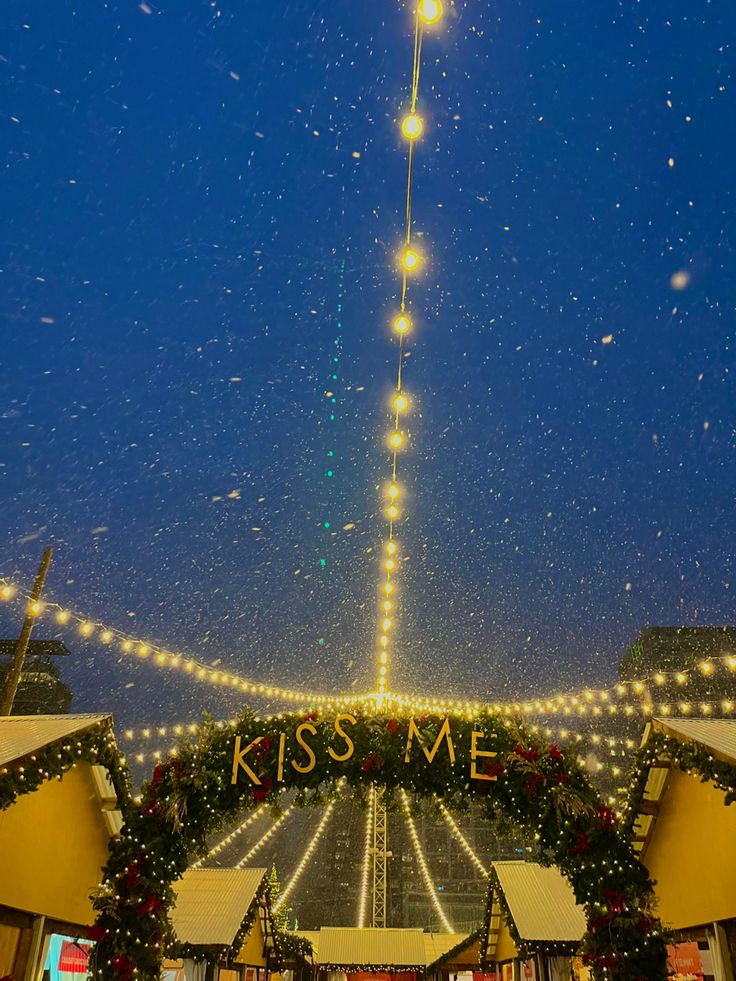 the entrance to kiss me is decorated with christmas lights and garlands, as snow falls on the ground