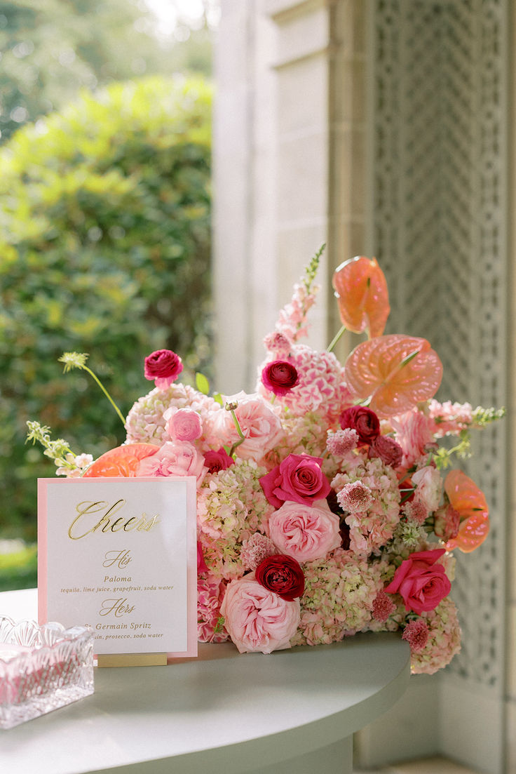 a bouquet of pink and white flowers on a table with a card next to it